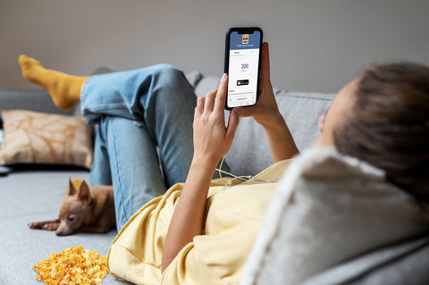 Woman lounging on couch with popcorn and dog while using phone